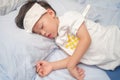 Asian 3 - 4 years old toddler boy gets high fever lying on bed with cold compress, wet washcloth on forehead to relieve pain