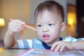Asian 2 - 3 years old toddler boy looking at pencil while writing / drawing, Preschooler doing homework
