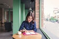 Asian yong woman in the cafe near the window, thinking and writing something. Royalty Free Stock Photo