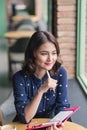 Asian yong woman in the cafe near the window, thinking and writing something. Royalty Free Stock Photo