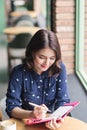 Asian yong woman in the cafe near the window, thinking and writing something. Royalty Free Stock Photo