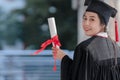 Asian young beautiful graduate female student with University degree turn back standing and holding diploma in hand and smiling Royalty Free Stock Photo