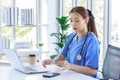Asian young beautiful professional successful female doctor in blue uniform with stethoscope sitting smiling taking coffee break Royalty Free Stock Photo