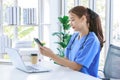 Asian young beautiful professional successful female doctor in blue uniform with stethoscope sitting smiling taking coffee break Royalty Free Stock Photo