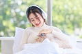 Asian young beautiful teenager girl owner in turtleneck sweater wearing headphones listening to music smiling on the bed Brush cat Royalty Free Stock Photo