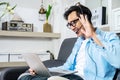 Asian young business man is wearing headphones video call conference with laptop computer raise hand saying hi team at home Royalty Free Stock Photo