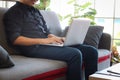 Asian young businessman typing on keyboard laptop computer while sitting on sofa couch in his apartment, freelancer working online Royalty Free Stock Photo