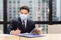 Asian young businessman wear protective mask using digital tablet and writing data on paper work in office.