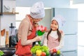 Asian young cheerful female chef housewife mother and little girl daughter wears white tall cook hat and apron standing smiling Royalty Free Stock Photo