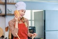 Asian young cheerful female housewife chef wearing white tall cook hat and apron standing smiling holding baguette bread and Royalty Free Stock Photo