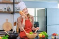 Asian young cheerful female housewife chef wearing white tall cook hat and apron standing smiling holding baguette bread and Royalty Free Stock Photo