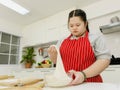 Asian young chubby down syndrome autistic autism girl pastry chef model wearing red apron standing threshing pulling bakery flour