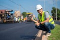 Asian young civil engineer showing confidence with thumb raised at road construction site with Asphalt paver & road roller & dump Royalty Free Stock Photo