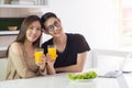 Asian young couple holding a glass of fresh orange juice for health with vegetable salad, laptop, and a smartphone. Royalty Free Stock Photo