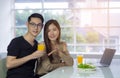 Asian young couple holding a glass of fresh orange juice for health with vegetable salad, laptop, and a smartphone Royalty Free Stock Photo