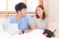 Asian young couple with man using laptop computer and searching internet and woman reading notebook on bed at bedroom Royalty Free Stock Photo