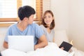 Asian young couple with man using laptop computer and searching internet and woman reading notebook on bed Royalty Free Stock Photo