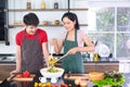 Asian young couple`s in apron, make cooking together. Woman mix salad dressing with vegetable in big bowl. Royalty Free Stock Photo