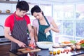 Asian young couple`s in apron, make cooking together. Woman mix salad dressing with vegetable in bowl. Royalty Free Stock Photo