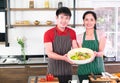 Asian young couple`s smiling, happiness in apron, make cooking together in kitchen. Showing big bowl of vegetable salad. there ar Royalty Free Stock Photo