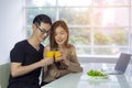 Asian young couple sitting in the kitchen and holding a glass of fresh orange juice for health with vegetable salad a laptop Royalty Free Stock Photo