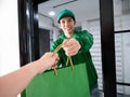 Asian young delivery man in green uniform jacket smile and send shopping paper bag to customer who purchased order online look