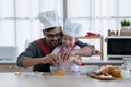 Asian young father with beard and little mixed race cute daughter with apron and chef hat smiling and cracking an egg in a bowl Royalty Free Stock Photo