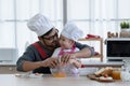 Asian young father with beard and little mixed race cute daughter with apron and chef hat smiling and cracking an egg in a bowl Royalty Free Stock Photo