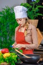 Asian young female chef housewife wears white tall cook hat and apron standing smiling on smartphone call holding wooden spoon Royalty Free Stock Photo