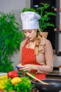 Asian young female chef housewife wears white tall cook hat and apron standing smiling on smartphone call holding wooden spoon Royalty Free Stock Photo
