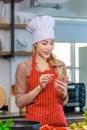 Asian young female chef housewife wears white tall cook hat and apron standing smiling on smartphone call holding wooden spoon Royalty Free Stock Photo