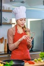 Asian young female chef housewife wears white tall cook hat and apron standing smiling on smartphone call holding wooden spoon Royalty Free Stock Photo