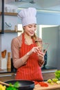 Asian young female chef housewife wears white tall cook hat and apron standing smiling on smartphone call holding wooden spoon Royalty Free Stock Photo