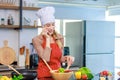 Asian young female chef housewife wears white tall cook hat and apron standing smiling on smartphone call holding wooden spoon Royalty Free Stock Photo