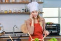 Asian young female chef housewife wears white tall cook hat and apron standing smiling on smartphone call holding wooden spoon Royalty Free Stock Photo