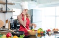 Asian young female chef housewife wears white tall cook hat and apron standing smiling on smartphone call holding wooden spoon Royalty Free Stock Photo