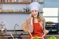 Asian young female chef housewife wears white tall cook hat and apron standing smiling on smartphone call holding wooden spoon Royalty Free Stock Photo