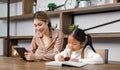 Asian young female housewife mother tutor teacher sitting smiling on table in living room holding tablet computer pointing Royalty Free Stock Photo