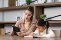 Asian young female housewife mother tutor teacher sitting smiling on table in living room holding tablet computer pointing Royalty Free Stock Photo