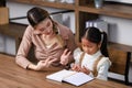 Asian young female housewife mother tutor teacher sitting smiling on table in living room at home teaching little cute Royalty Free Stock Photo