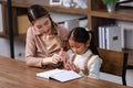 Asian young female housewife mother tutor teacher sitting smiling on table in living room at home teaching little cute Royalty Free Stock Photo