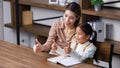 Asian young female housewife mother tutor teacher sitting smiling on table in living room at home teaching little cute Royalty Free Stock Photo