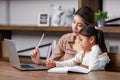 Asian young female housewife mother tutor teacher sitting smiling on table in living room using notebook computer pointing Royalty Free Stock Photo