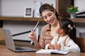 Asian young female housewife mother tutor teacher sitting smiling on table in living room using notebook computer pointing Royalty Free Stock Photo
