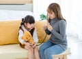 Asian young female mother sitting on cozy sofa smiling holding teddy bear doll playing doctor patient with little cute daughter gi