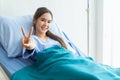 Asian young Female patients wearing blue shirts lying in the bed showing two-finger symbols with a bright face Have better