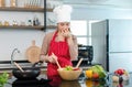 Asian young frowning face female housewife chef wearing white tall cook hat and apron standing holding hand closing nose mixing