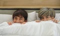 Asian young gay couple with smiley face hiding under white blanket in bed Royalty Free Stock Photo