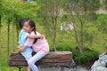 Asian young girl child embracing little boy while sitting on wooden bench in the park Royalty Free Stock Photo