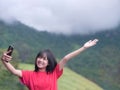 Asian young girl taking selfie photos on her smartphone from a scenic viewpoint with majestic panorama of mountain canyon